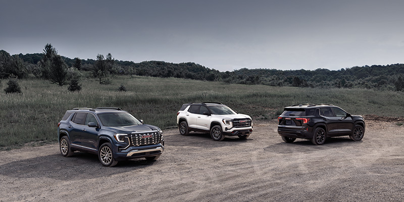 Three GMC Acadia SUVs on gravel with a grassy hill