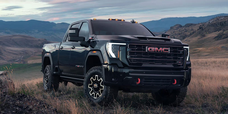 Black GMC Sierra HD pickup truck parked on a grassy hillside with mountains in the background.